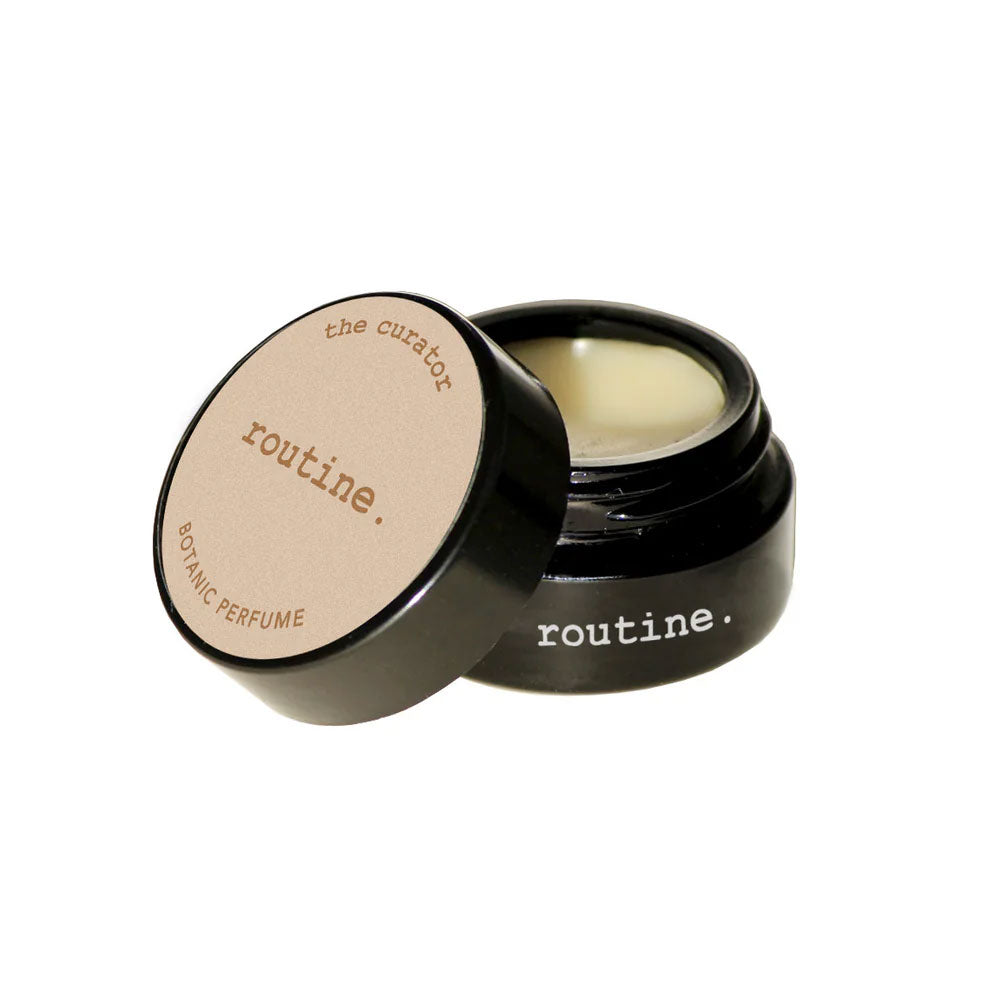 Routine The Curator solid perfume - black glass jar with cream label open revealing golden balm texture