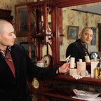 A man holding The Curator deodorant stick in a vintage bedroom setting showing sustainable paper packaging.