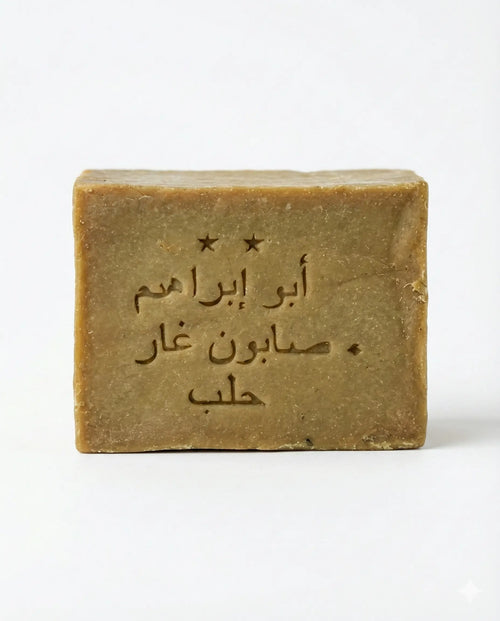 Front view of an olive-tan Aleppo soap bar stamped with Arabic text and two stars on a plain white background.