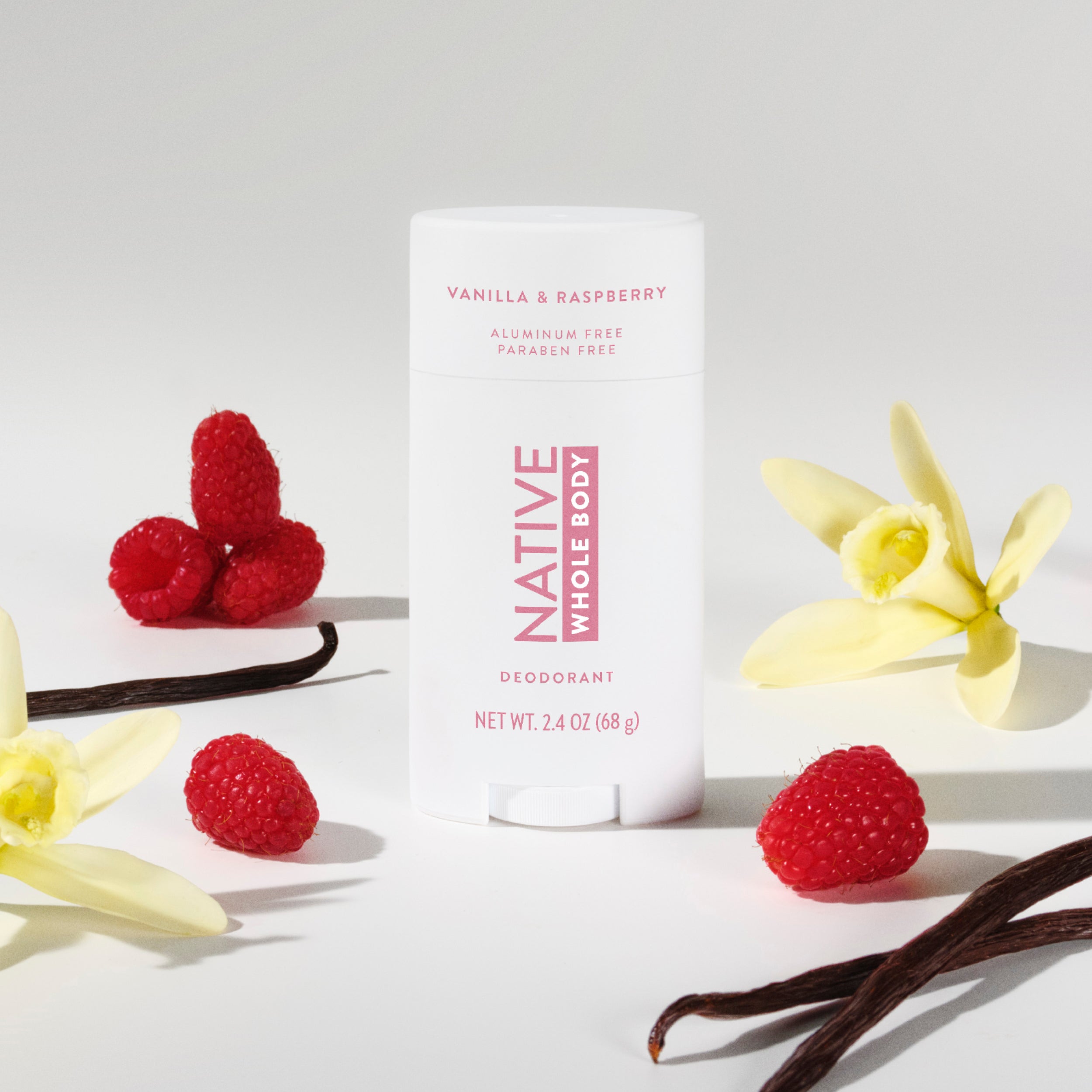 Native Whole Body Deodorant container stands among fresh red raspberries, yellow vanilla flowers, and dark bean pods.