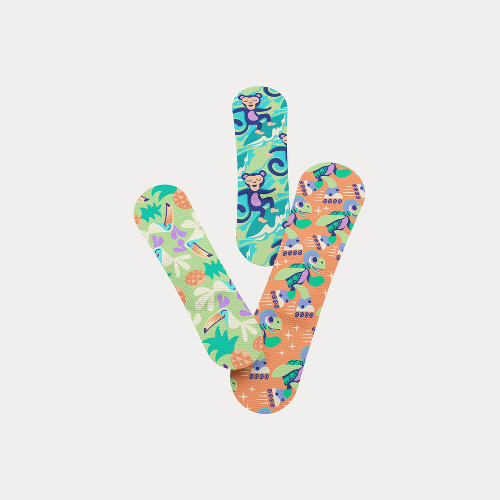 Three fabric bandages in tropical monkey, roller-skating turtle, and toucan patterns overlapping in a V-shape.