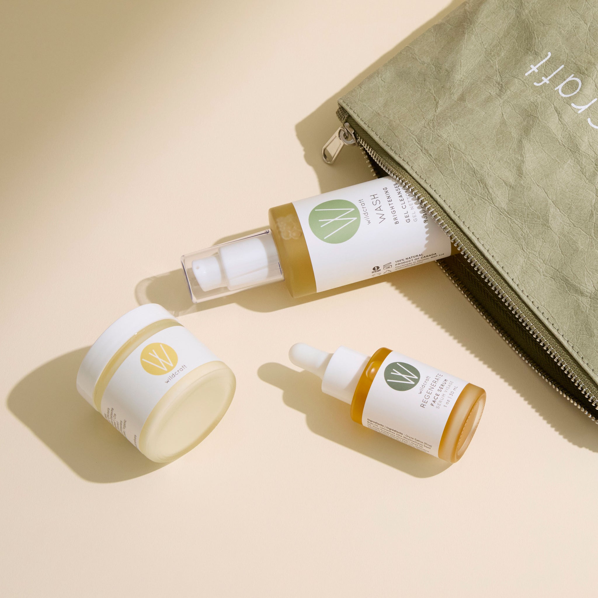Three Wildcraft skincare bottles lie on a beige surface next to an open olive green zippered pouch.