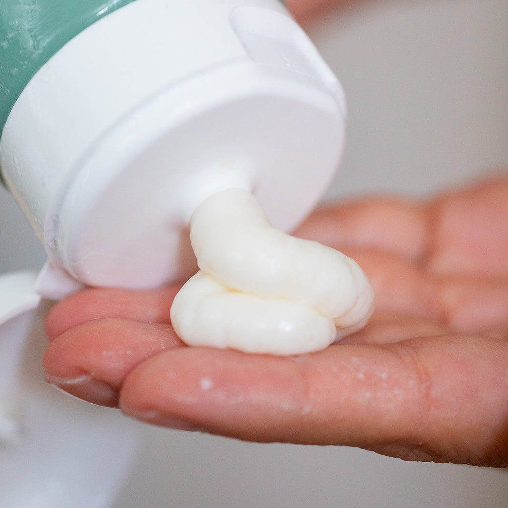 Thick white cream conditioner being squeezed from a tube with a white cap onto an open palm.
