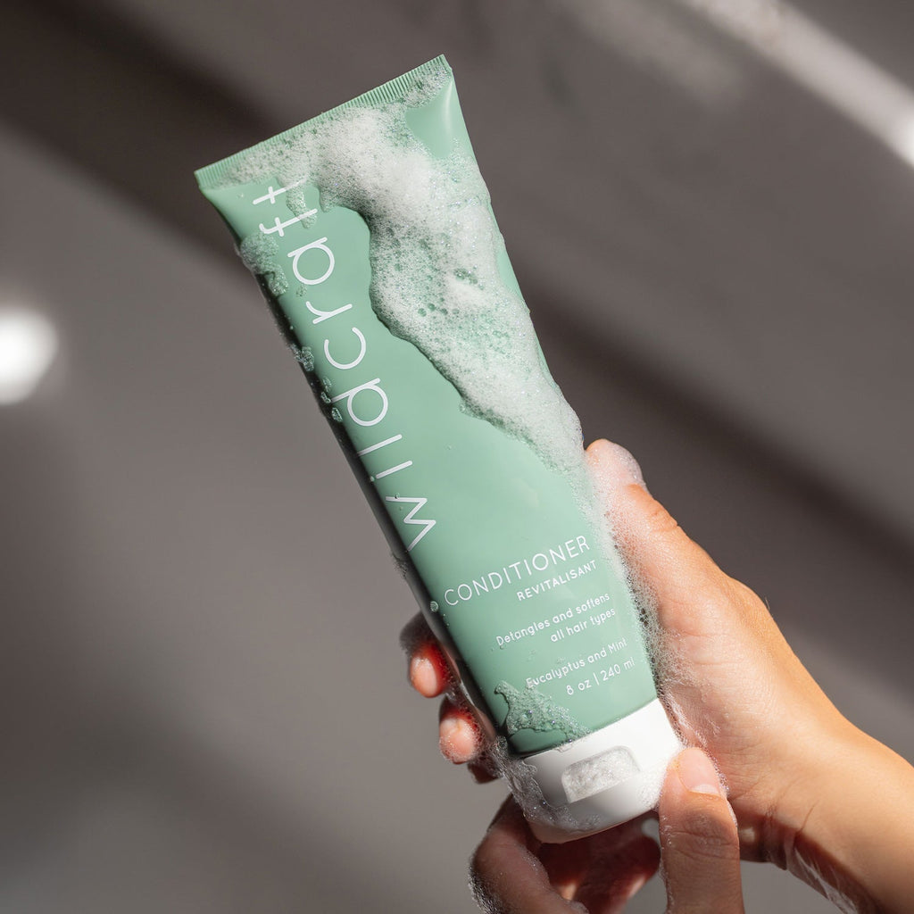 Soapy hands hold the green Wildcraft conditioner tube covered in white bubbly lather.
