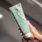 Soapy hands hold the green Wildcraft conditioner tube covered in white bubbly lather.