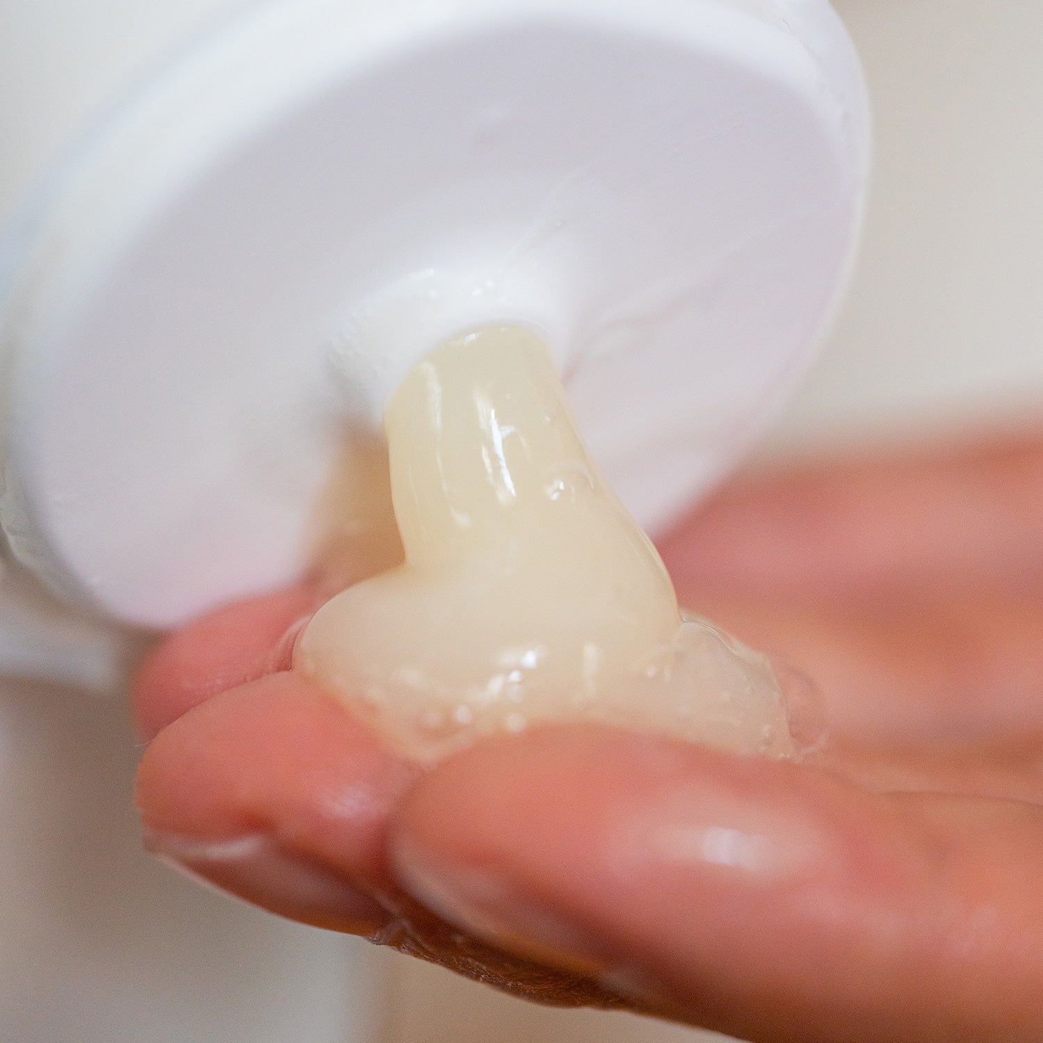 A thick, semi-translucent pale yellow gel shampoo squeezes from a white bottle cap onto a person's palm.