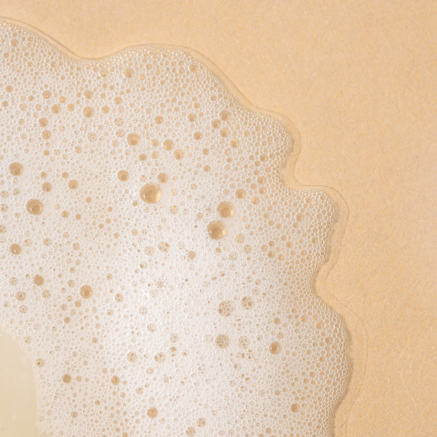 A close-up texture shot of fine white soapy lather and bubbles spread over a textured beige surface.