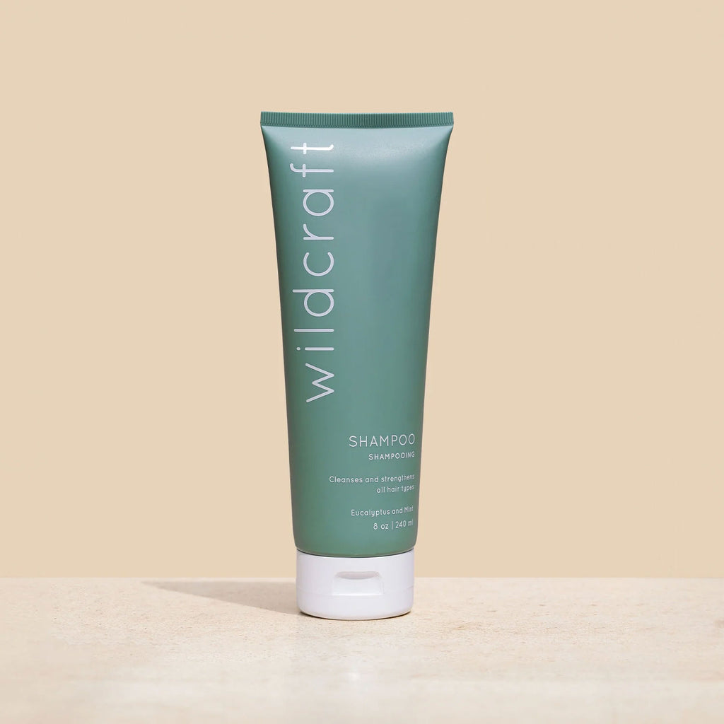A matte sage green tube of Wildcraft shampoo stands on a sandy stone surface against a beige background.