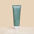 A matte sage green tube of Wildcraft shampoo stands on a sandy stone surface against a beige background.
