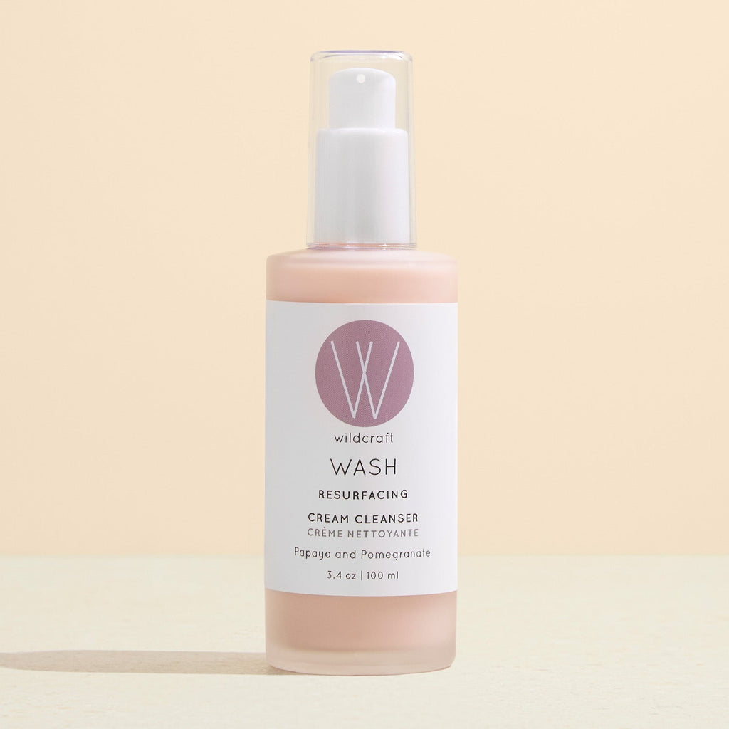A frosted glass pump bottle of peach-coloured Wildcraft Wash Cream Cleanser standing on a pale beige surface.