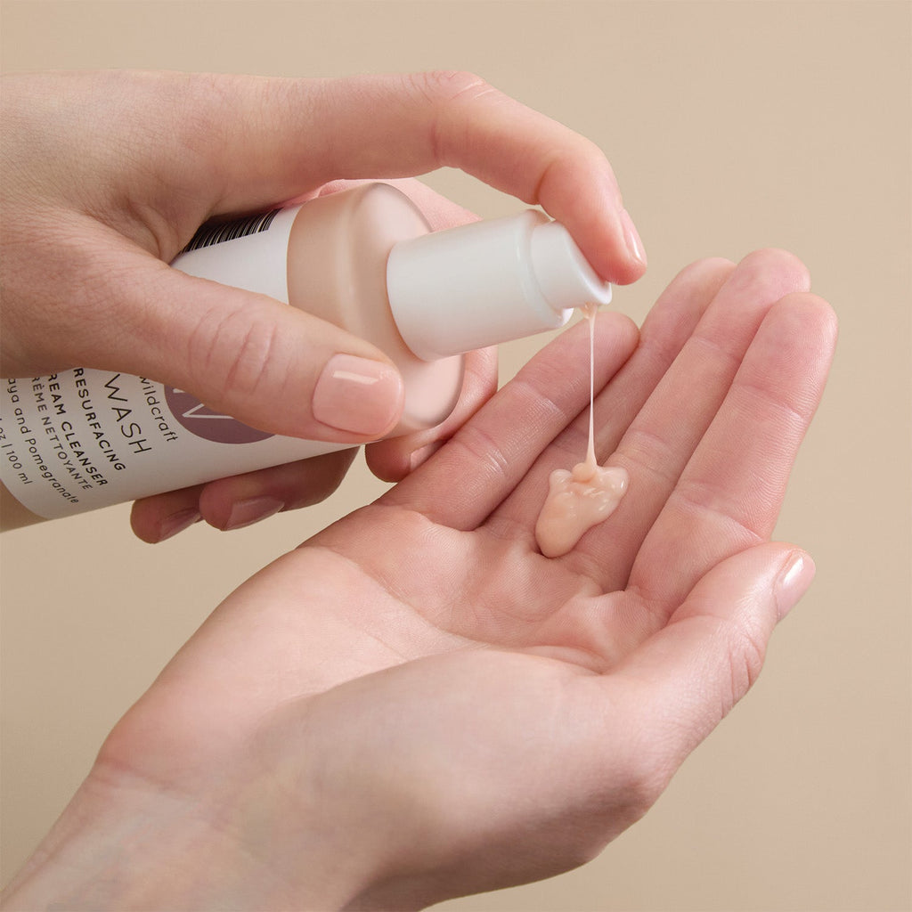 A person pumps a dollop of pale peach cream cleanser from a Wildcraft bottle into their open palm.