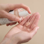 A person pumps a dollop of pale peach cream cleanser from a Wildcraft bottle into their open palm.