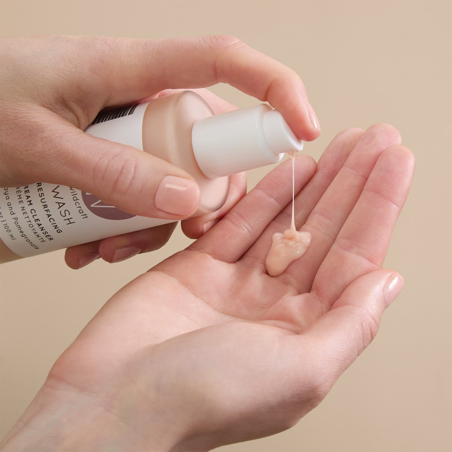 A person pumps a dollop of pale peach cream cleanser from a Wildcraft bottle into their open palm.