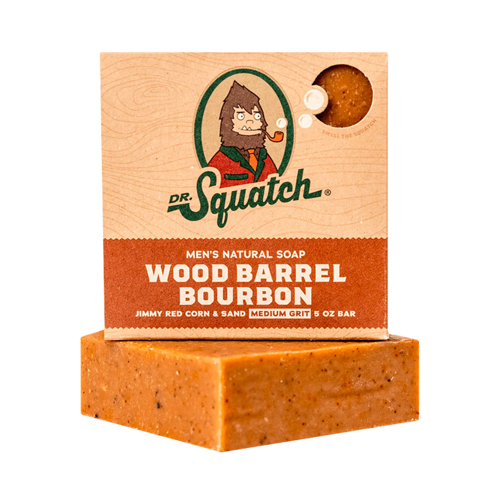 A rectangular bar of soap with a textured brown color, placed in front of its packaging which features the Dr. Squatch logo and the text 'MEN'S NATURAL SOAP WOOD BARREL BOURBON'.