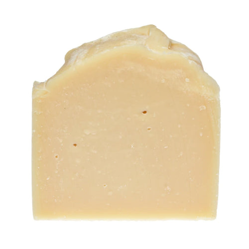 An unwrapped beige bar of soap with an uneven, hand-cut top and a slightly textured surface against a white background.