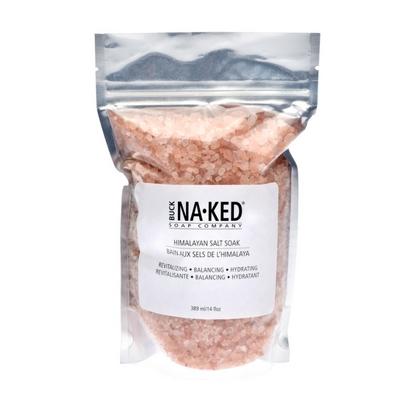 Pink coarse bath salt crystals fill a clear stand-up pouch with a white Buck Naked Soap Company label.