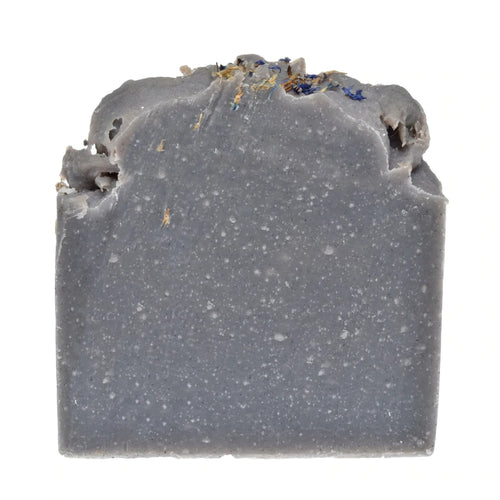 Unwrapped indigo soap bar with a speckled grey-blue body and a rough-cut top edge sprinkled with dried flower petals.