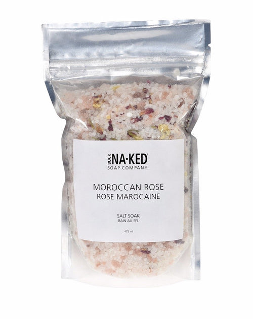 A clear resealable pouch of Buck Naked Moroccan Rose bath salt showing pink and white crystals with dried flower petals.